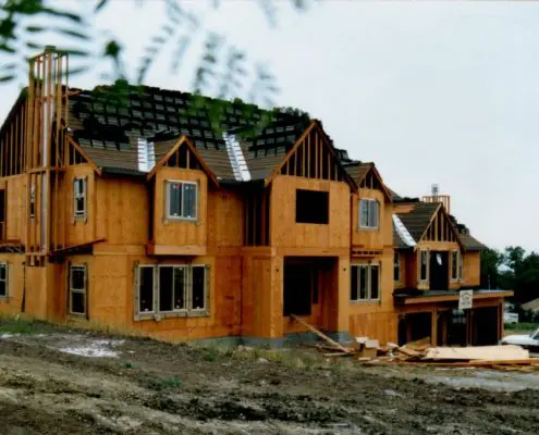 Large residential house under construction with plywood sheathing, exposed wood framing, and a partially installed roof