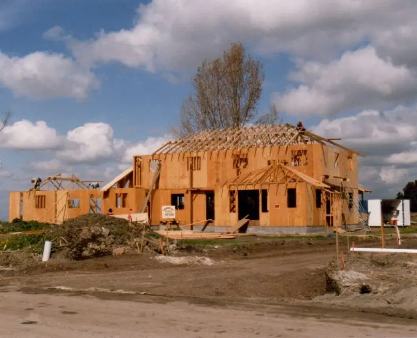 Partially constructed wooden house on a construction site under a cloudy sky