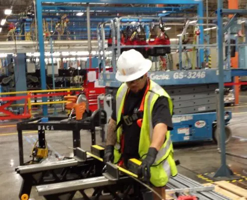 Construction worker measuring metal tubing on a workbench inside an industrial facility