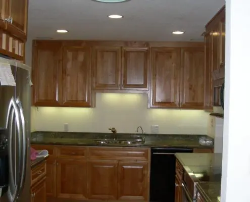 Modern kitchen interior with wooden cabinets, granite countertops, stainless steel appliances, and recessed ceiling lights