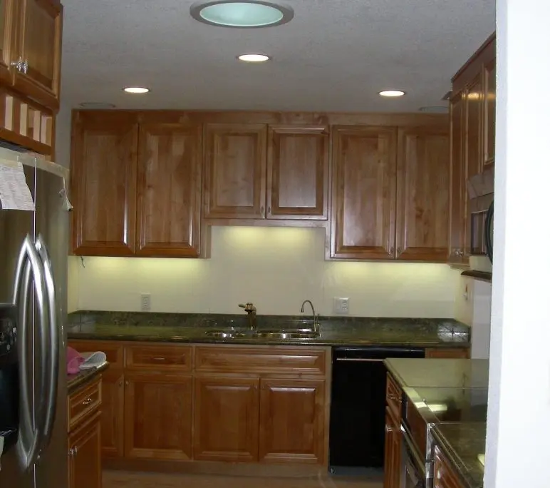 Modern kitchen interior with wooden cabinets, granite countertops, stainless steel appliances, and recessed ceiling lights