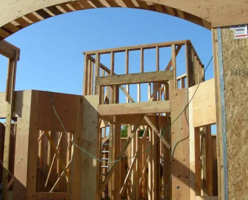 Framing stage of residential construction with wooden arch by L.E. Baca Construction