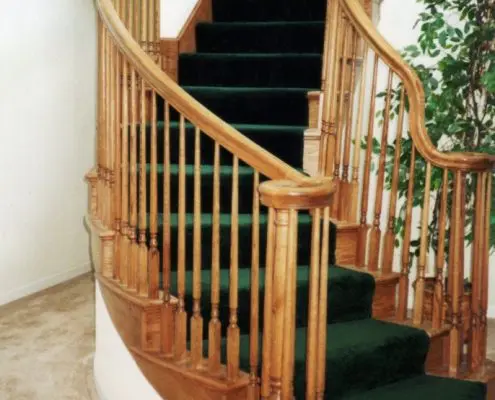Elegant wooden spiral staircase with green carpet by L.E. Baca Construction