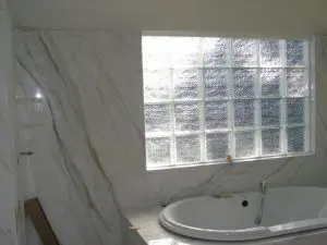 New bathroom construction with marble walls, built-in soaking tub, and frosted glass block window