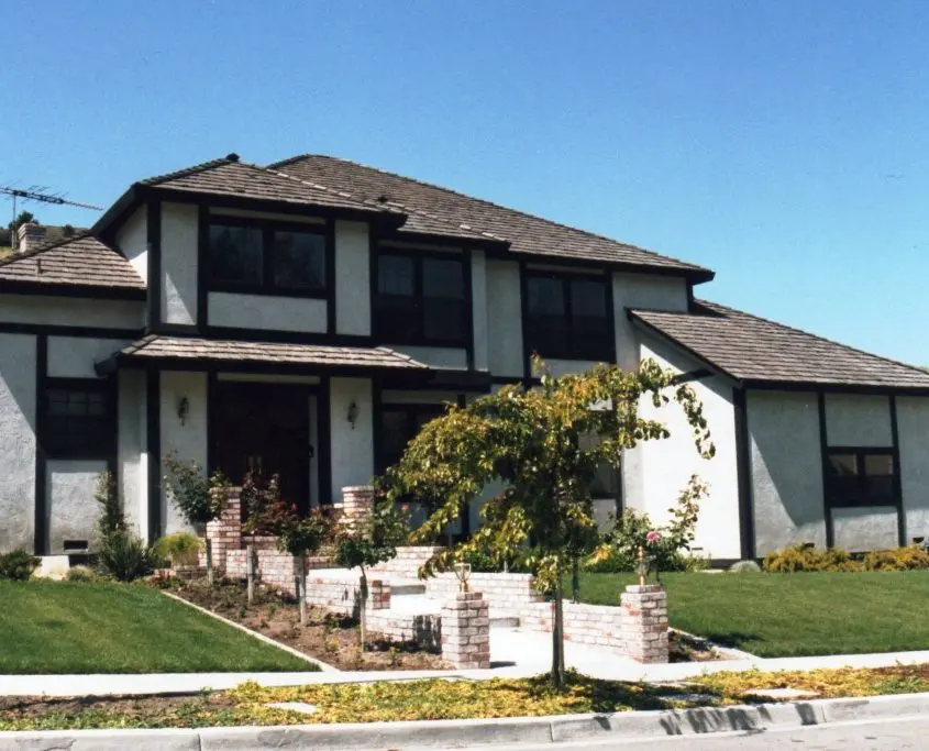 Modern residential home with a white facade and contrasting dark brown accents, set against a clear blue sky