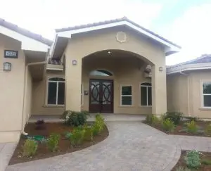 Front exterior of new stucco home with arched entryway and double wooden doors with decorative glass inserts.