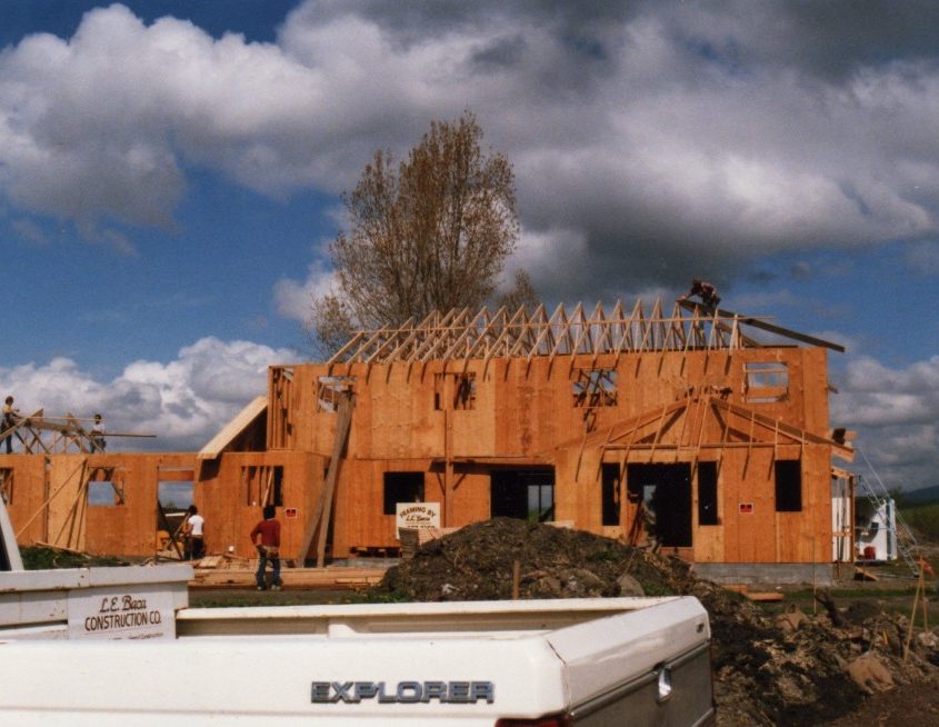 Early stage of house construction, showing the skeletal wood structure and roof framing with L.E. Baca Construction Co