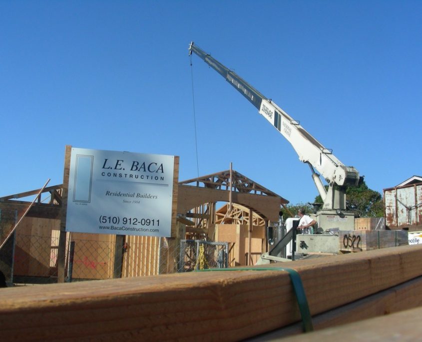 Residential construction site with crane lifting materials and L.E. Baca Construction sign in foreground