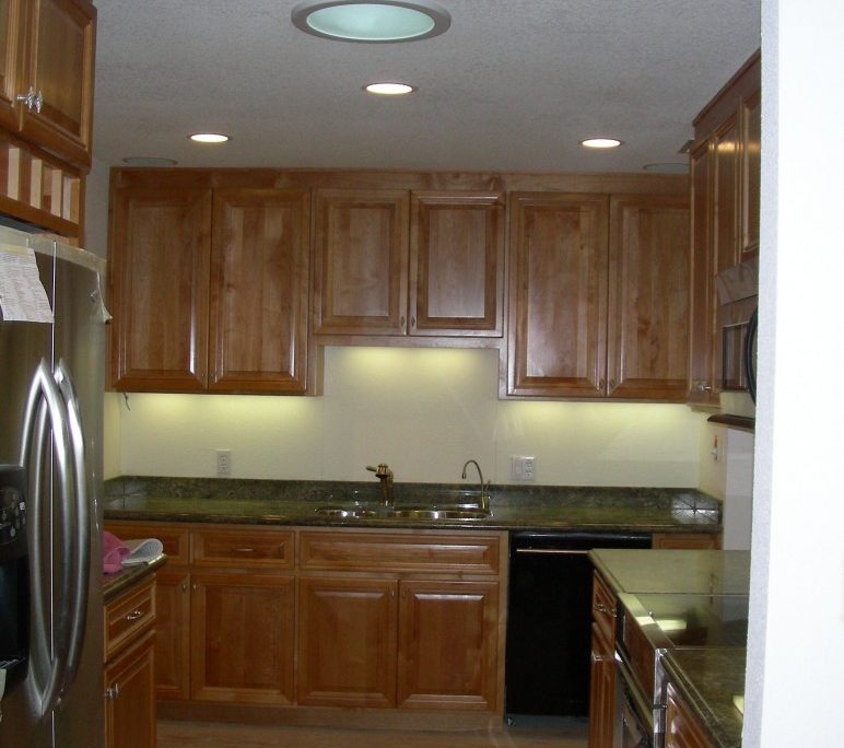 Modern kitchen interior with wooden cabinets, granite countertops, stainless steel appliances, and recessed ceiling lights