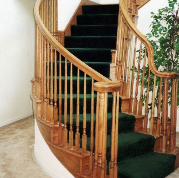 Elegant wooden spiral staircase with green carpet by L.E. Baca Construction