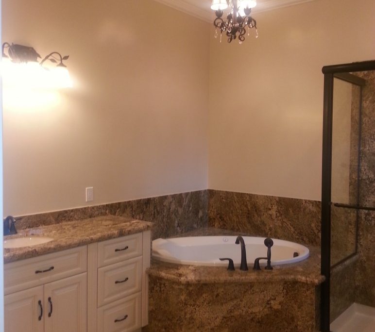 Luxurious bathroom remodel with granite tub surround and chandelier lighting