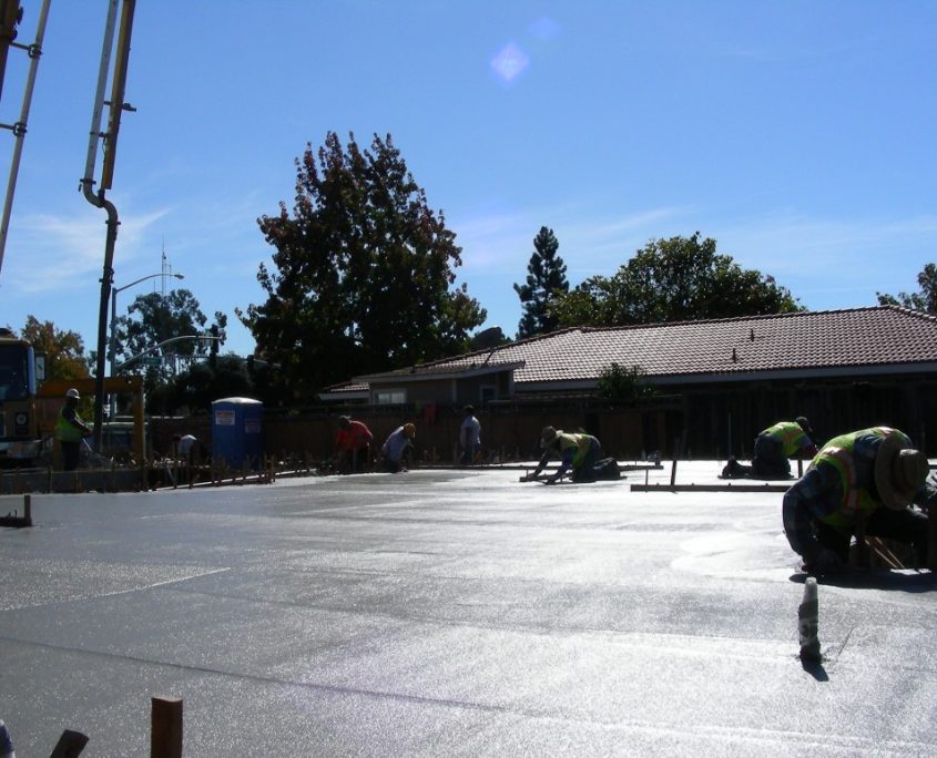 Outdoor construction site with multiple workers pouring and smoothing wet concrete under a clear sky